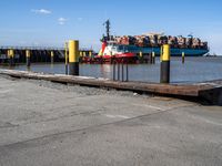 a large blue barge is next to the dock in the harbor, with people standing on the docks edge