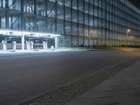 a skateboarder skates in a deserted street at night as an empty building is lit up