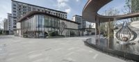 the outside courtyard of a large hotel that features glass walls and a circular fountain in the center