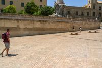 people sitting on benches and talking to each other in an open courtyard area, with the town's clock tower and building in the background