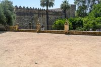 an old stone building is surrounded by palm trees and bushes near the gate to the entrance of the park