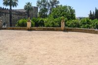 an old stone building is surrounded by palm trees and bushes near the gate to the entrance of the park