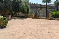 an old stone building is surrounded by palm trees and bushes near the gate to the entrance of the park