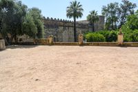 an old stone building is surrounded by palm trees and bushes near the gate to the entrance of the park