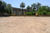 an old stone building is surrounded by palm trees and bushes near the gate to the entrance of the park