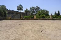 an old stone building is surrounded by palm trees and bushes near the gate to the entrance of the park