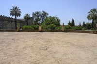 an old stone building is surrounded by palm trees and bushes near the gate to the entrance of the park