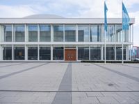 the entrance to an industrial building with glass walls and doors is shown from outside on a grey concrete surface with a bench and chairs