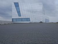 a building with white paint on it in front of a brick walkway under a gray cloudy sky