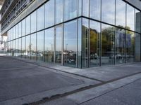 a side view of a building with glass on a street by the water's edge