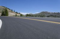 a curve in the middle of a road with two yellow lines between it and mountains behind