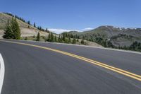 a curve in the middle of a road with two yellow lines between it and mountains behind