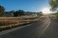 the sun shines over a country road in the countryside near tall grass and trees