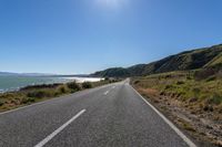 an empty country road leads to the ocean and a mountain with high peaks in the background