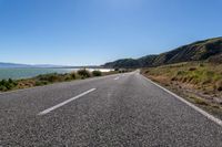 an empty country road leads to the ocean and a mountain with high peaks in the background