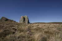 large rock at the top of a grass field in the countryside and a blue sky above