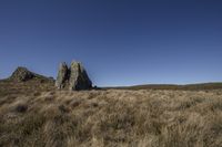 large rock at the top of a grass field in the countryside and a blue sky above