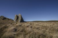 large rock at the top of a grass field in the countryside and a blue sky above