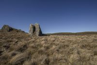 large rock at the top of a grass field in the countryside and a blue sky above