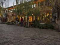 a couple walking outside of a store next to plants and trees on the street,