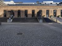 an empty courtyard with stairs and steps in front of it and a brick building behind it