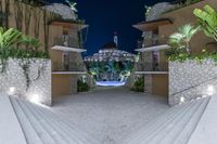 a courtyard area at night, showing a fountain and stone steps leading up to some palm trees