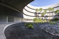 a courtyard of rocks and gravel next to palm trees and plants on the ground in front of a building