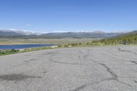 the intersection has patches of cracks in concrete and a view of mountains, lake, and town