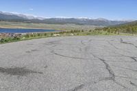 the intersection has patches of cracks in concrete and a view of mountains, lake, and town