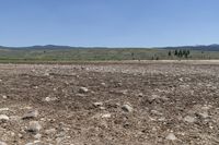 a field with rocks and dirt on a sunny day with mountains in the background at the bottom