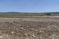 a field with rocks and dirt on a sunny day with mountains in the background at the bottom