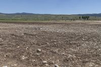 a field with rocks and dirt on a sunny day with mountains in the background at the bottom