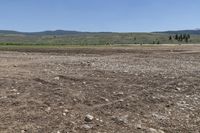 a field with rocks and dirt on a sunny day with mountains in the background at the bottom