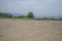 an empty area with some trees in the distance and mountains in the distance through it