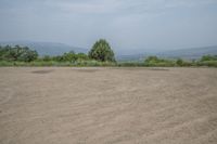 an empty area with some trees in the distance and mountains in the distance through it