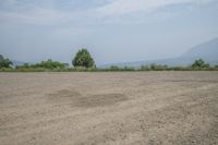 an empty area with some trees in the distance and mountains in the distance through it