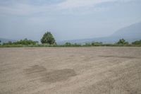 an empty area with some trees in the distance and mountains in the distance through it