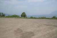 an empty area with some trees in the distance and mountains in the distance through it