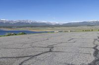 a car that is parked in a parking lot next to a lake with mountains in the background