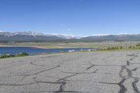 a car that is parked in a parking lot next to a lake with mountains in the background