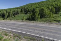 motorcycle rider on roadway overlooking green hills with trees in background and clear blue sky above