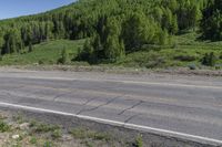 motorcycle rider on roadway overlooking green hills with trees in background and clear blue sky above