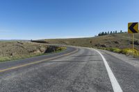 an empty road with a yellow traffic sign on it and mountains in the background with blue sky