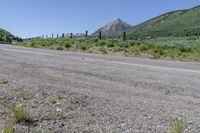 a stop sign on the side of a road beside a field and a mountain in the background