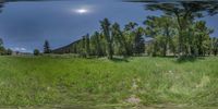 a field with grass and trees under a cloudy sky in this picture is a panoramic