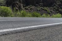 a lone motorcycle is on an empty road near rocks and mountains at a distance and trees all around