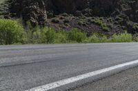 a lone motorcycle is on an empty road near rocks and mountains at a distance and trees all around