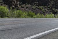 a lone motorcycle is on an empty road near rocks and mountains at a distance and trees all around