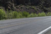 a lone motorcycle is on an empty road near rocks and mountains at a distance and trees all around