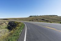 a yellow road next to the hills and fields, on a clear day with blue skies